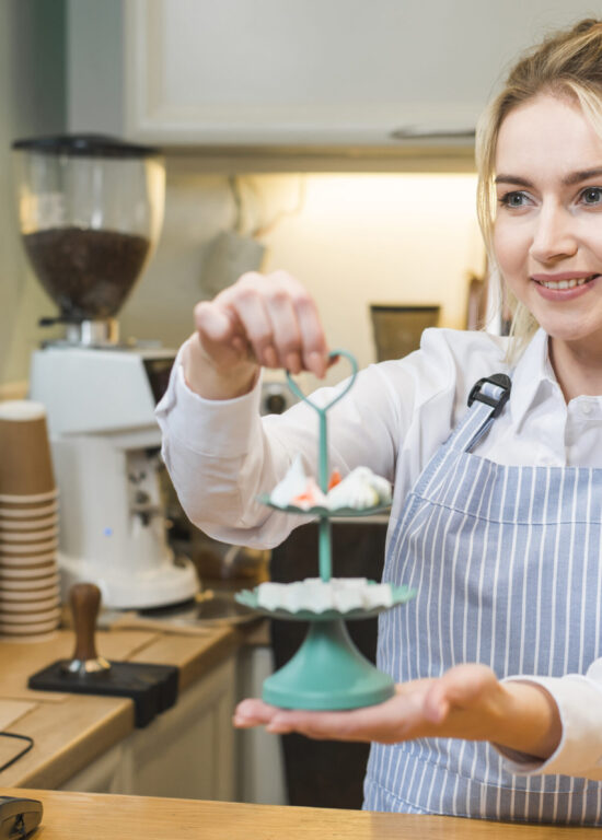 smiling-young-woman-holding-meringue-sugar-cubes-three-tier-serving-tray-coffee-shop